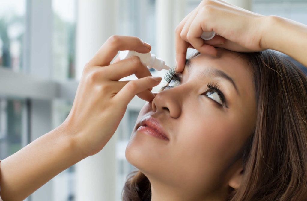 A woman putting eye drops in her eye to lubricate her eyes and relieve the discomfort caused by dry eye syndrome.