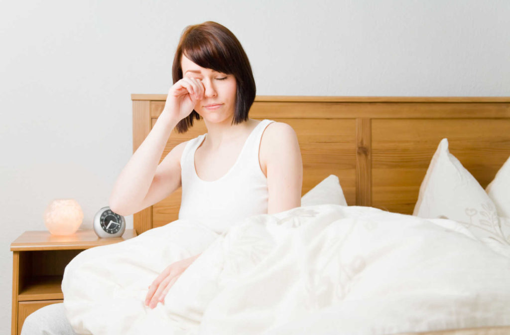 A woman waking up with dry eye and rubbing her eyes while sitting in bed.