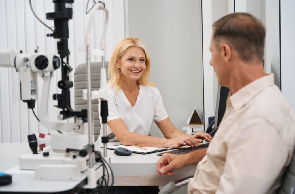 Smiling female optometrist sitting at a desk across from a male patient.