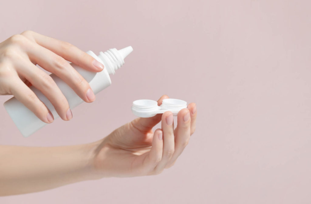 Hands holding a cleaning solution for contact lenses and a case for contact lenses.