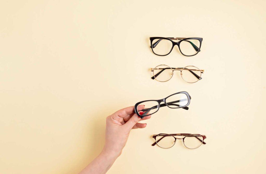 Four pairs of eyeglasses set out with a woman's hand reaching out holding one of the pairs.