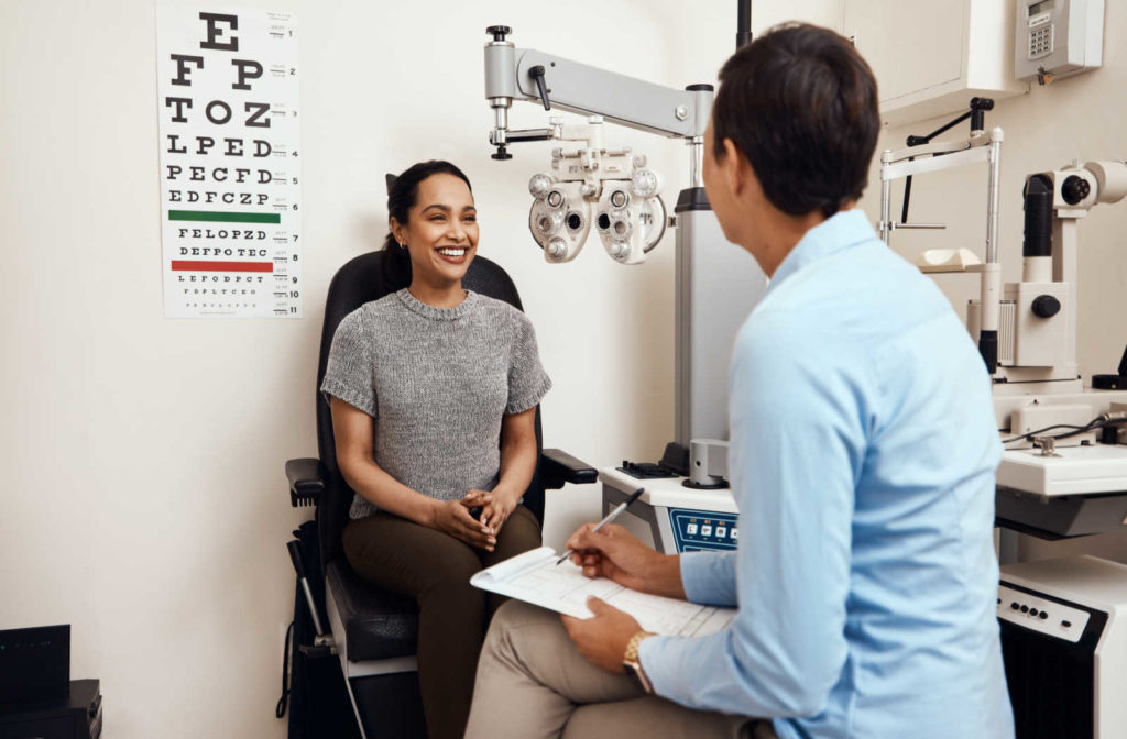A young woman sitting in an optometrist's office and smiling at her eye doctor.