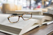 A pair of leopard print eyeglasses folded and sitting on top of an open book on a desk.