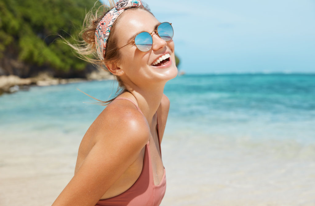 A happy young woman by the beach wearing a pair of UV protection sunglasses.