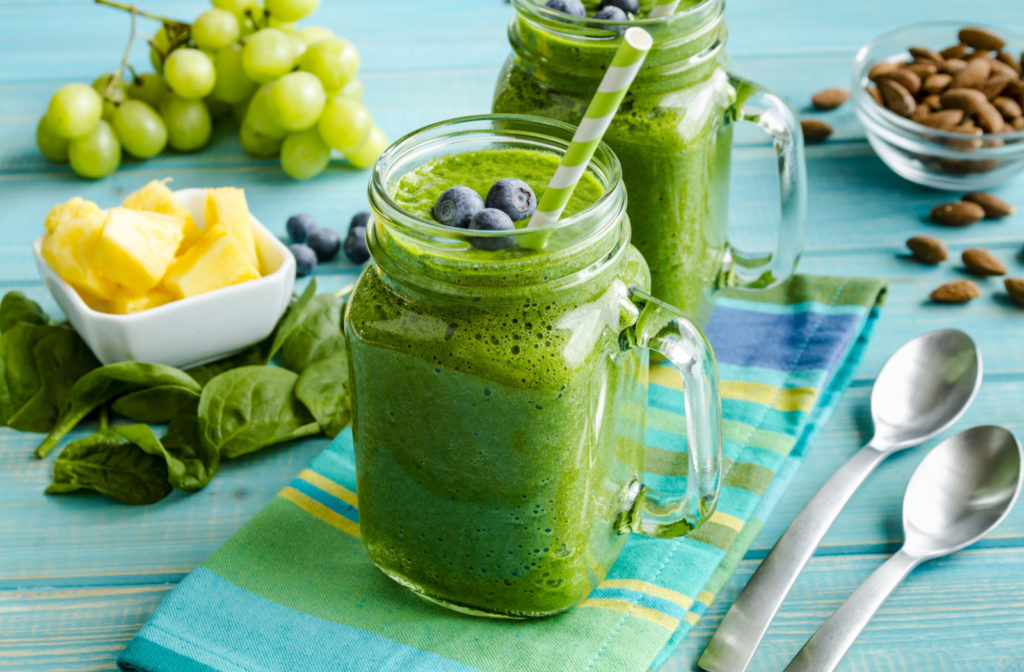 2 glass mason jars on a table, filled with delicious green smoothies and topped with blueberries.