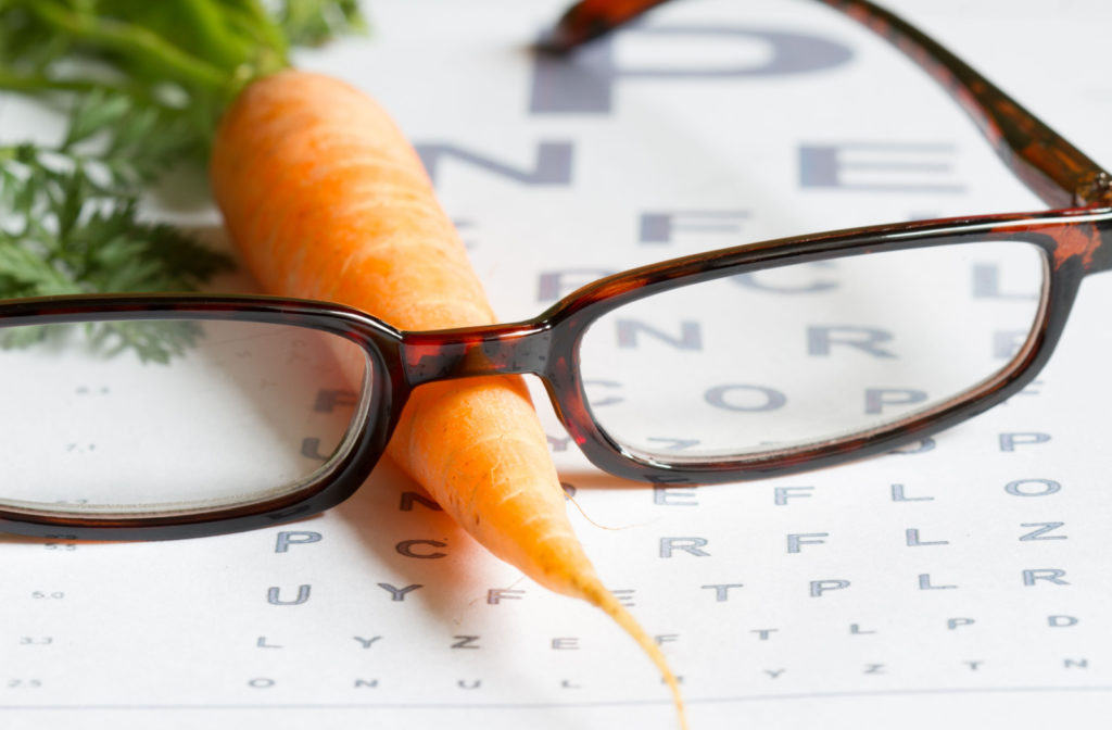A pair of eyeglasses resting next to fresh carrots on an eye chart