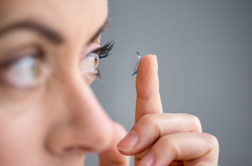 Close-up of a woman holding a contact lens up to her left eye with her left index finger.