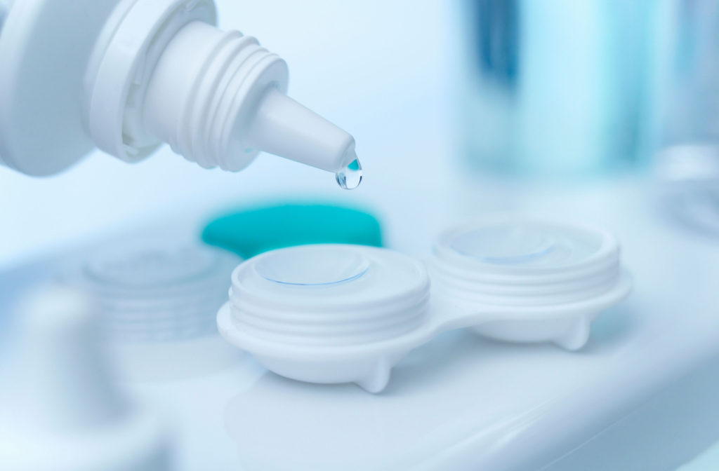 A close-up of a pair of contact lenses on a protective case being cleaned using a disinfecting solution.