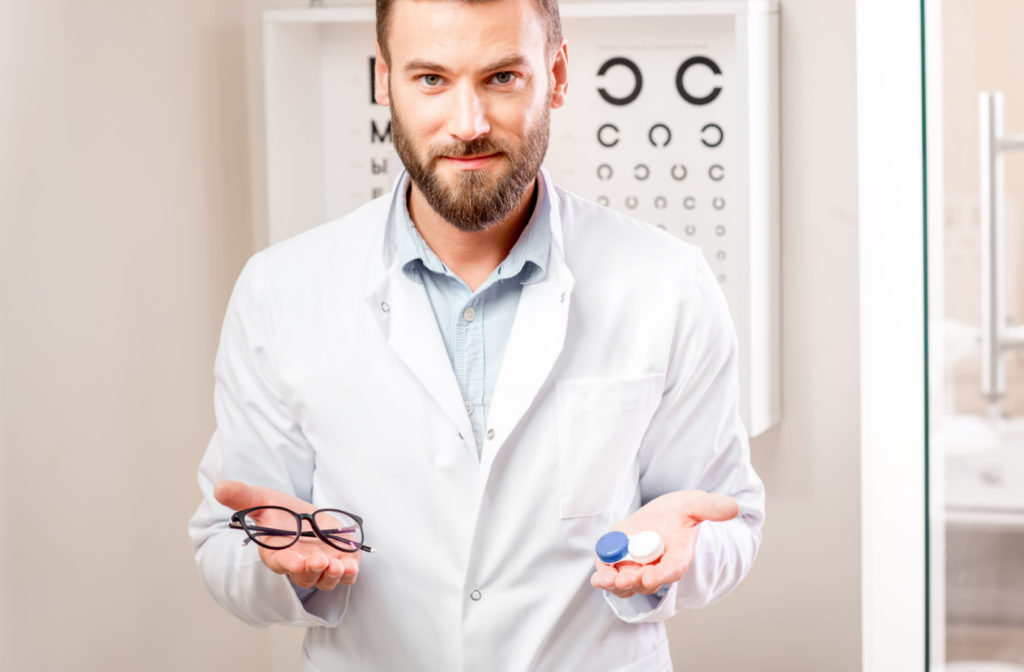 An optometrist presenting a pair of eyeglasses and a container of contact lenses in his eye clinic.