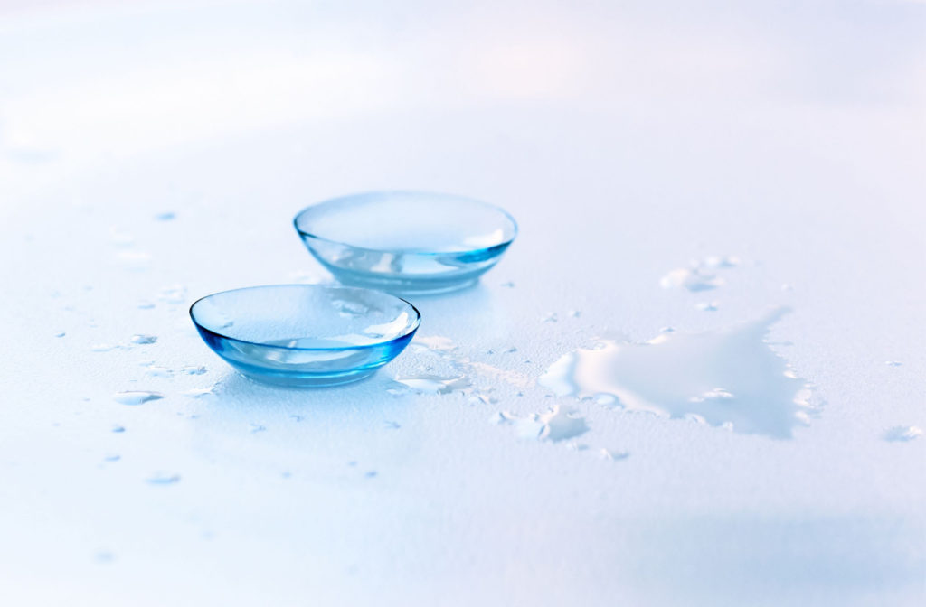 Close-up of a pair of soft contact lenses on surface with a few drops of contact lens solution.